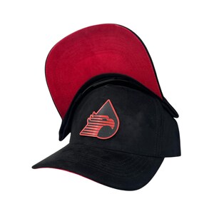 May include: Black baseball cap with a red interior and a red and black logo on the front. The cap has a curved brim and ear flaps. The logo is a stylized design.