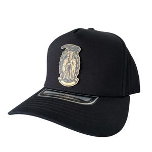 Könnte beinhalten: Schwarze Baseballkappe mit flachem Schirm. Auf der Kappe befindet sich ein goldfarbenes Emblem eines Sensenmanns mit einer Sense. Das ovale Emblem weist detaillierte Merkmale auf. Die Kappe besteht aus robustem Material und hat eine strukturierte Passform.