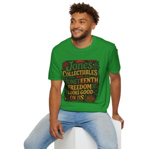 May include: A green t-shirt with the text "Jones Collectibles and Juneteenth Freedom Looks Good On Us" in a decorative frame. The shirt is short-sleeved and the person is wearing blue jeans.