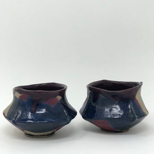 May include: Two small ceramic bowls with a dark purple glaze and a blue and white pattern. The bowls have a unique, irregular shape.