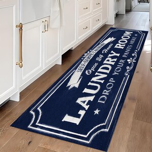 May include: A rectangular navy blue runner rug featuring white decorative borders and text that reads: SELF-SERVE LAUNDRY, Open 24 Hours, LAUNDRY ROOM, and DROP YOUR PANTS HERE, accented with stars and scrollwork designs on the edges.