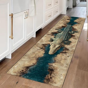 Può includere: Tappeto rettangolare con un'illustrazione dettagliata di un alligatore in un fiume. Il tappeto presenta un design a fiume blu con sponde rocciose marroni e beige. L'alligatore è verde e beige.