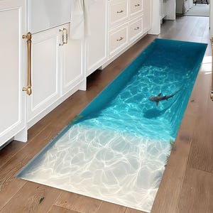 May include: A blue and white beach-themed rug with a shark swimming in the water. The rug is placed on a wooden floor in a hallway.