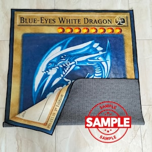 Może przedstawiać: Prostokątny dywan z "Blue-Eyes White Dragon" z kolekcjonerskiej gry karcianej Yu-Gi-Oh!. Dywan ma ilustrację niebieskiego smoka na niebieskim tle, z tekstem i symbolami gwiazd karty. Dywan jest prostokątny z czarną obw&oacute;dką.