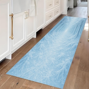 May include: A rectangular blue runner rug with a winter forest design. The rug features a light blue background with a pattern of white tree branches, creating a tunnel effect. The rug is placed on a wooden floor.
