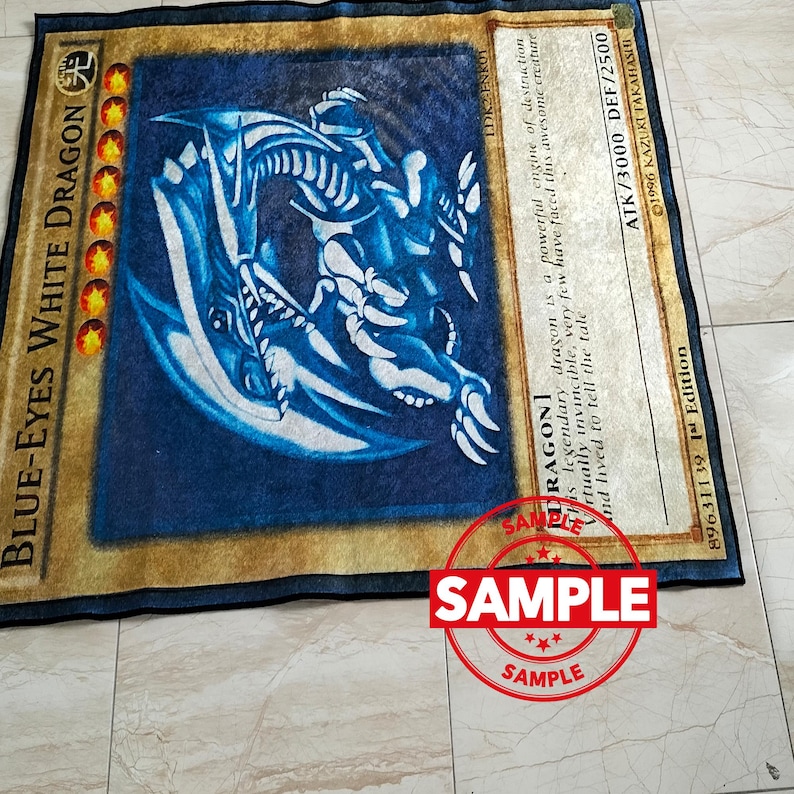 Może przedstawiać: Prostokątny dywan z Białym Smokiem Błękitnookim z gry karcianej Yu-Gi-Oh!. Dywan ma niebieskie tło z ilustracją białego smoka, złotą obw&oacute;dką i szczeg&oacute;łami karty.