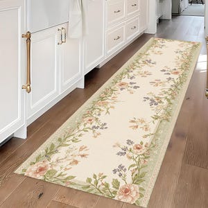 Peut inclure: Un tapis de couloir rectangulaire à motifs floraux avec un fond crème et une bordure de fleurs vertes, roses et violettes. Le tapis est posé sur un parquet dans une cuisine.