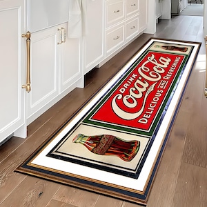 May include: A vintage-style Coca-Cola rug with a red and white logo and a bottle of Coca-Cola. The rug has a black and gold frame and is on a wooden floor.