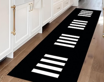 May include: Black runner rug with white crosswalk design. The rectangular rug is placed on a hardwood floor in a kitchen setting. The rug's design features three sets of white stripes, resembling a pedestrian crosswalk.