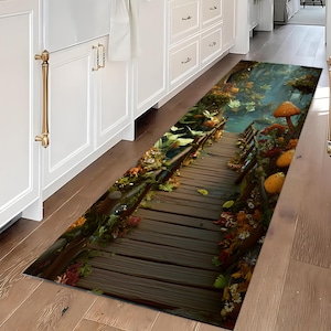May include: A rectangular kitchen rug featuring a detailed illustration of a wooden bridge over a stream. The rug has a naturalistic design with autumn foliage, mushrooms, and a serene, misty background. The color palette includes browns, greens, and oranges.