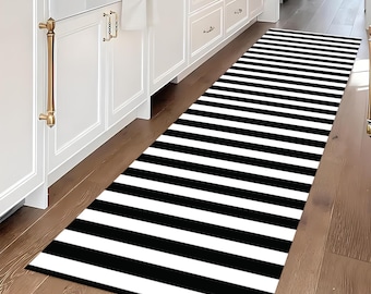 May include: Black and white striped runner rug with a modern design. The rug is placed in a hallway with white cabinets and hardwood floors.