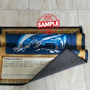 Może przedstawiać: Prostokątny dywan z niebiesko-białym wzorem smoka i napisem "BLUE EYES WHITE DRAGON". Dywan ma czarną obw&oacute;dkę i antypoślizgowy sp&oacute;d. Na dywanie znajduje się stempel z napisem "SAMPLE".
