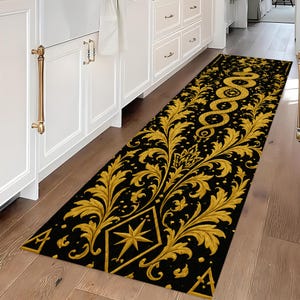 May include: A long rectangular runner rug featuring a black background with a repeating gold-coloured pattern of ornate acanthus leaves, a coiled snake, and a central star inside a diamond shape, positioned on a wooden floor in a kitchen.