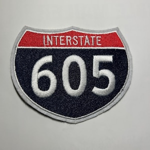 May include: Embroidered patch in the shape of a shield, with the text "INTERSTATE" in white on a red bar, and the number "605" in white on a navy blue background. The patch has a white border.