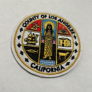 Puede incluir: Parche bordado con el sello del condado de Los Ángeles. El parche circular tiene un fondo blanco con un borde dorado y texto negro. El sello incluye una mujer, un barco y otros símbolos.