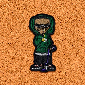 Peut inclure: Un écusson brodé représentant un personnage de dessin animé portant un sweat à capuche vert, un pantalon noir et des baskets. Le personnage a le teint hâlé, les cheveux foncés et tient un petit gobelet blanc avec un liquide violet qui se renverse.