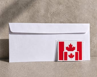 May include: A crisp white business-sized envelope positioned horizontally. Attached to the lower right corner is a clear plastic sleeve containing two rectangular stickers, each featuring the red and white Canadian flag with a central maple leaf.
