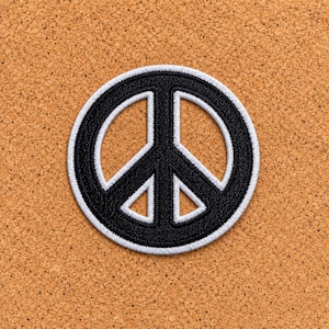 May include: A circular embroidered patch featuring a black peace sign symbol. The design consists of a thick black circular border and internal black lines forming the peace emblem, all outlined with a crisp white stitched border.