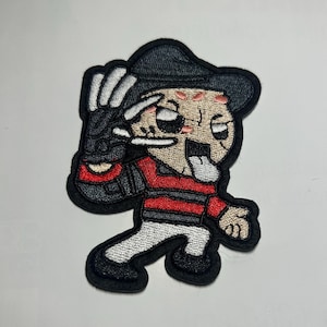 May include: Embroidered patch featuring a cartoon character with a black hat and glove, red and black striped shirt, and a tongue sticking out. The patch has a black border and white accents.