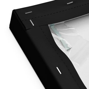 Op de afbeelding: Close-up van een zwart canvas frame met een wit canvas dat erin is gespannen. Het frame is vastgezet met nietjes en een metalen ophanghaak is zichtbaar.