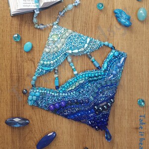 Peut inclure: Un collier de perles bleu et turquoise avec un motif en forme de vague. Le collier est composé de perles de différentes tailles et formes, et il a un pendentif qui pend du bas. Le collier est présenté sur une surface en bois avec d'autres perles bleues et turquoise.