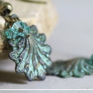 May include: A pair of earrings featuring a teal and green shell design with light blue crystal accents.