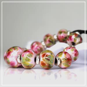 May include: A bracelet featuring round glass beads with a marbled pattern of pink, green, and white colors. The beads are separated by small, cylindrical silver-toned metal spacers and are strung on a black cord, creating a colorful accessory.