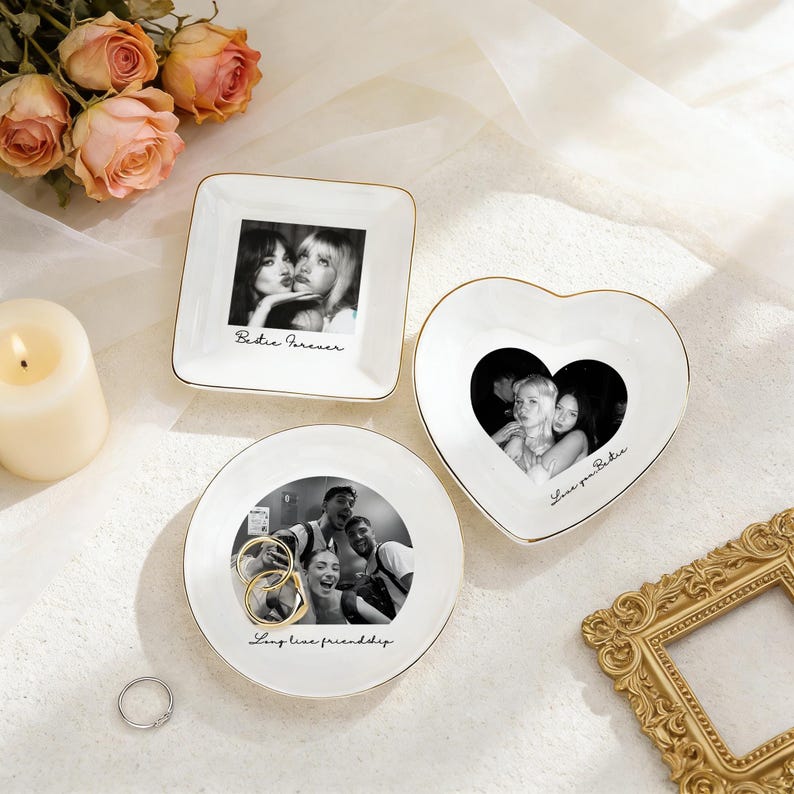 K&ouml;nnte beinhalten: Drei wei&szlig;e Keramik-Schmuckschalen mit goldenen R&auml;ndern. Eine quadratische Schale zeigt ein Schwarz-Wei&szlig;-Foto und den Text "Bestie Forever". Eine herzf&ouml;rmige Schale und eine runde Schale zeigen ebenfalls Fotos und Text. Eine Kerze und Rosen sind im Hintergrund.