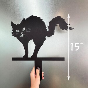 May include: Black metal cat silhouette with an arched back and a menacing expression. The cat is 15 inches tall and mounted on a horizontal bar with a vertical handle. A Halloween-themed decoration.