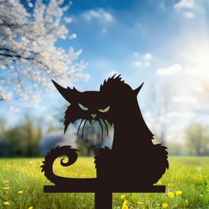May include: Black metal cat silhouette garden stake with an angry expression. The cat has pointed ears, a curled tail, and a crossbar for easy placement in the yard. The background features a sunny sky and green grass.