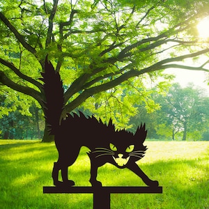May include: A black metal cat garden stake with a menacing expression, green eyes, and a snarling mouth. The cat has a spiky back and a long, upright tail. The stake is placed in a grassy yard with trees in the background.