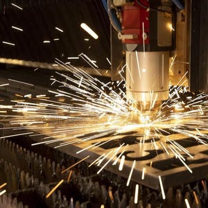 May include: A close-up of a laser cutter in operation, creating sparks as it cuts through a metal sheet. The machine is red and silver, with a focused beam of light. The metal sheet is dark, with cut-out shapes.