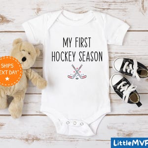 a teddy bear sitting next to a baby's first hockey season shirt