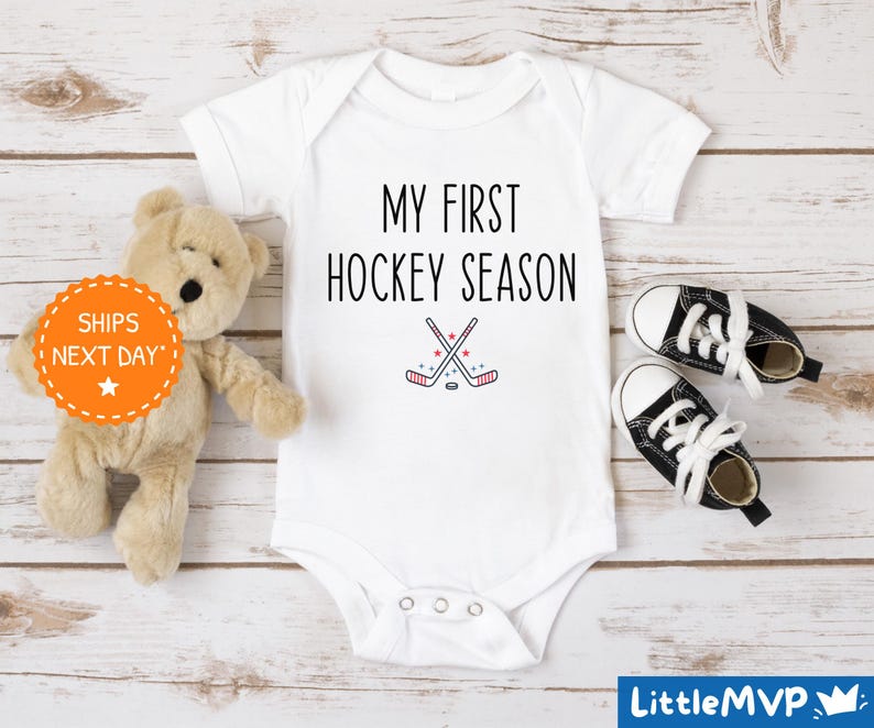 a teddy bear sitting next to a baby's first hockey season shirt