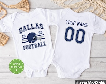 Pode incluir: Dois bodies brancos para bebê. Um body tem o texto "Dallas Football" com um gráfico de capacete de futebol. O outro body tem o texto "Your Name 00".