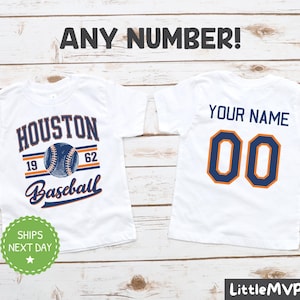 May include: White t-shirt with a baseball design featuring the text "Houston Baseball" and a baseball with the numbers 19 and 62. The back of the shirt has the text "Your Name" and the number 00.