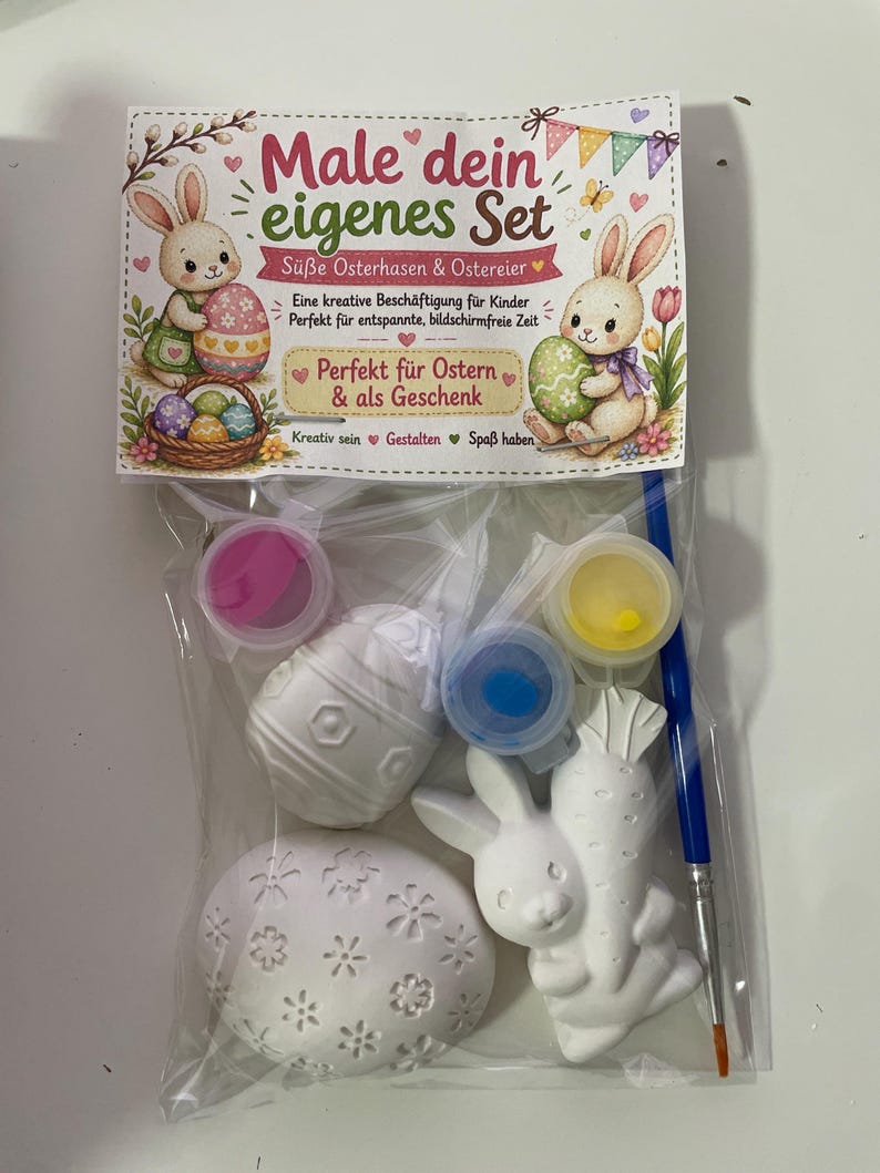 Puede incluir: Un kit de manualidades de Pascua con pintura, un pincel y figuras de Pascua de cer&aacute;mica. El kit incluye un conejito, una zanahoria y huevos. El embalaje tiene texto en alem&aacute;n e ilustraciones de conejos y huevos.