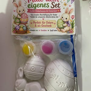 Puede incluir: Un juego de Pascua para pintar en una bolsa de pl&aacute;stico transparente. El juego incluye una figura de conejito, dos figuras en forma de huevo, botes de pintura y un pincel. El embalaje presenta ilustraciones de conejitos y huevos, con texto en alem&aacute;n.