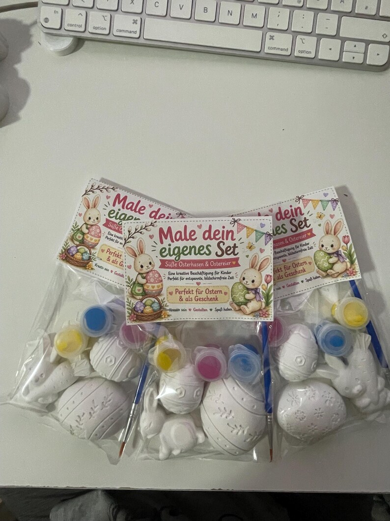 Puede incluir: Tres juegos de pintura con tem&aacute;tica de Pascua. Cada juego incluye huevos y conejos de Pascua de cer&aacute;mica blanca, botes de pintura de varios colores y pinceles. El texto "Male dein eigenes Set" es visible.