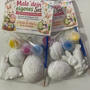 Puede incluir: Juego de pintura de Pascua para pintar. El juego incluye huevos de Pascua y figuras de conejos de cer&aacute;mica blanca, botes de pintura y pinceles. El embalaje presenta ilustraciones de conejos y huevos, con texto en alem&aacute;n.