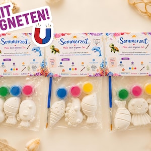 Può includere: Tre set di pittura fai-da-te con forme di creature marine, vasetti di vernice e pennelli. Ogni set include una tartaruga, un delfino e il testo "Sommerzeit". I set sono confezionati in sacchetti di plastica trasparente.