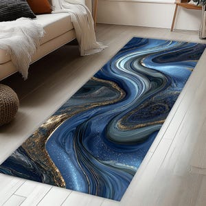 Könnte beinhalten: Ein rechteckiger Teppich mit einem fließenden, abstrakten Design in Blau-, Gold- und Grautönen. Das Muster ähnelt wirbelndem Marmor oder Flüssigkeit, mit goldenen Akzenten. Der Teppich liegt auf einem hellen Holzboden.