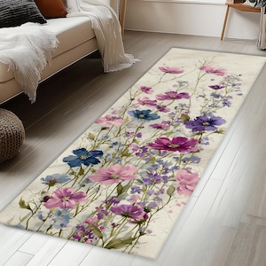 Peut inclure: Un tapis rectangulaire au fond crème orné d'un motif botanique de fleurs sauvages dans des tons de violet, rose et bleu. Le dessin floral présente diverses fleurs ressemblant à des cosmos et de fines tiges vertes réparties sur la surface.