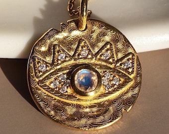May include: Gold necklace with a round pendant featuring an evil eye design with a moonstone center and clear crystal accents.