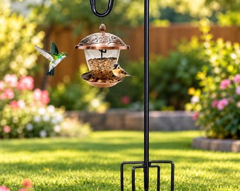 May include: A black metal shepherd's hook stand with a four-pronged base supports a hanging bird feeder. The feeder features a copper-colored lid with embossed leaf details, a clear glass reservoir filled with birdseed, and a copper tray.