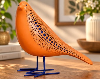 May include: A decorative bird figurine featuring a bright orange body with a perforated pattern revealing a deep blue interior. The bird stands on thin, straight blue metal legs and feet, creating a contrast between the orange and blue.