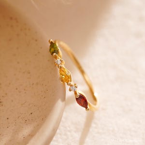 Peut inclure: Une bague en or ornée d'une rangée de pierres précieuses de forme marquise de couleurs verte, jaune et rouge, rehaussée de petites pierres blanches. La bague a un anneau fin et une finition polie.