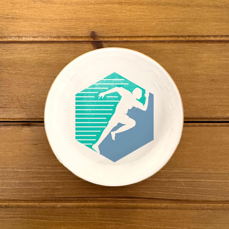 May include: White ceramic dish with a gold rim featuring a blue and green graphic of a runner in a hexagonal shape.
