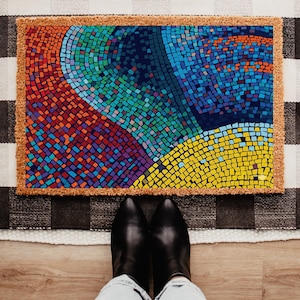 May include: Rectangular doormat with a mosaic design in shades of red, blue, green, and yellow. The mosaic pattern is framed by a natural brown border. The doormat is placed on a black and white checkered rug.