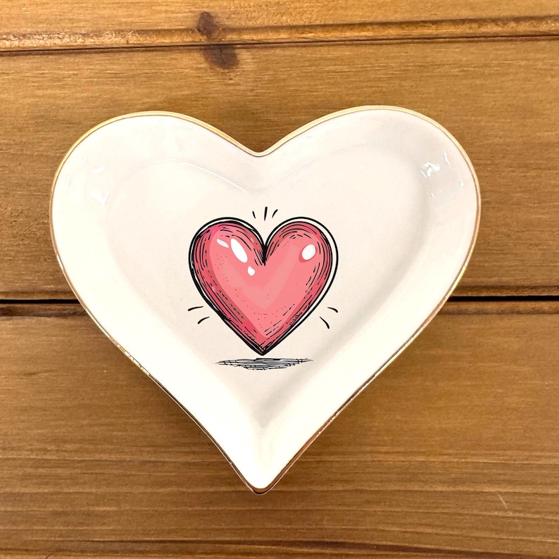 May include: White heart-shaped ceramic dish with a gold rim and a pink heart design in the center.